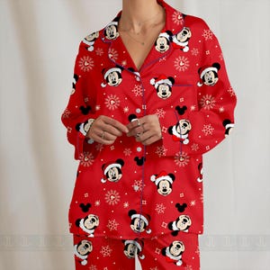 May include: Red pajama set featuring a pattern of Mickey Mouse in Santa hats and white snowflakes. The long-sleeved top has a notched collar and button-down front. The pajama set is made of a soft material.