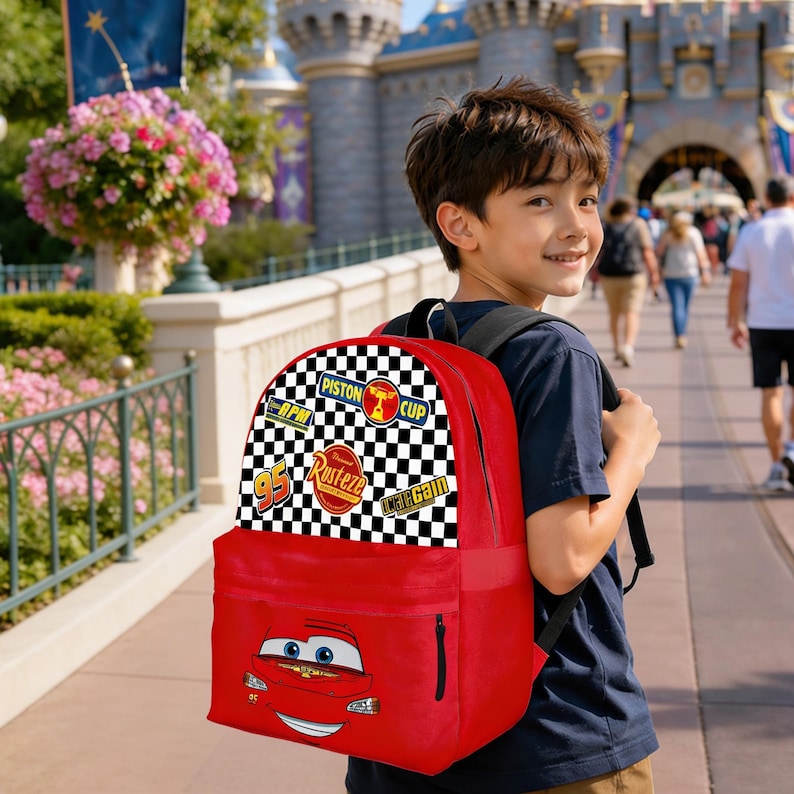 May include: A red backpack with a Lightning McQueen design from the Cars film. The top flap features racing patches and a chequered flag pattern. The backpack is worn by a person. The bag has a large front pocket.