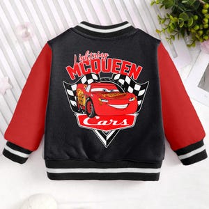 May include: Black and red bomber jacket with a red Lightning McQueen Cars graphic on the back. The jacket has white stripes on the sleeves and bottom.