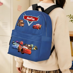 May include: A blue backpack with a Cars movie theme. The backpack has a front pocket and a top handle. The name "Sofia" is displayed in a red and white logo on the top. The backpack is being worn.