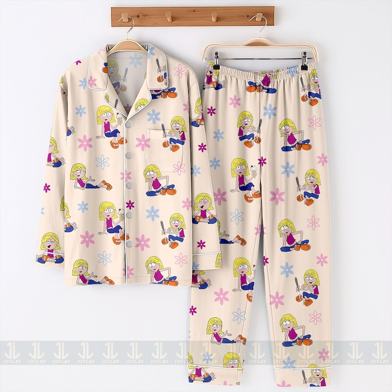 Pu&ograve; includere: Un completo pigiama beige con un'illustrazione a cartoni animati di una ragazza bionda che tiene in mano un gelato e un motivo floreale. Il set include una camicia abbottonata e pantaloni.