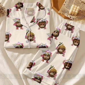 May include: A two-piece pajama set featuring a repeating pattern of a cartoon coconut character with a fierce expression. The pajamas are white with a contrasting white trim and buttons.