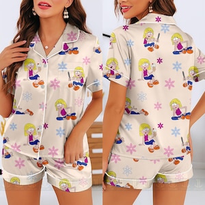 Pu&ograve; includere: Pigiama color crema con un design di personaggi dei cartoni animati e fiori. La maglia a maniche corte e i pantaloncini presentano un motivo ripetuto di una ragazza che tiene in mano un gelato e fiori. Il set ha finiture bianche.