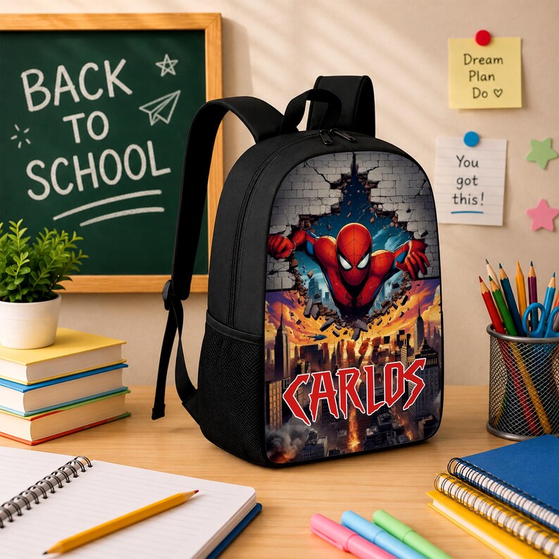 May include: A black backpack featuring a graphic print of a red and blue superhero bursting through a brick wall above a city skyline. The name Carlos is printed in large red letters at the bottom of the graphic. The bag has black straps.