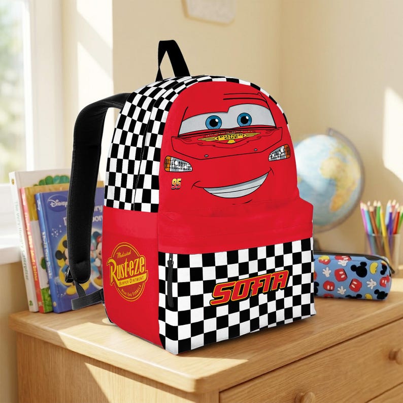 Peut inclure: Un sac &agrave; dos rouge avec Flash McQueen du film Cars. Le sac &agrave; dos pr&eacute;sente un motif &agrave; carreaux noir et blanc sur les c&ocirc;t&eacute;s et une grande image du personnage sur le devant. Le mot "SOFIA" est imprim&eacute; sur la poche avant.