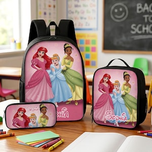 May include: A black backpack, lunch bag, and pencil case set featuring a pink background with illustrations of Ariel, Cinderella, and Tiana. The name Sophia is printed in white script on the pencil case and lunch bag, with a pink graphic design.