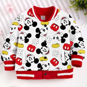 May include: White bomber jacket with a red collar and cuffs. The jacket features a repeating pattern of Mickey Mouse heads, gloves, and hats in red, black, and yellow.