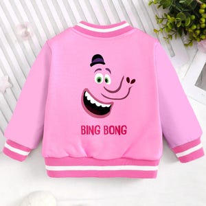 May include: Pink bomber jacket with a white stripe around the collar and cuffs. The jacket features a cartoon character with a hat and the text "Bing Bong" printed on the back.