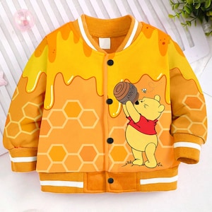May include: A yellow and orange bomber jacket with a Winnie the Pooh design. The jacket features a honey pot, honeycomb, and a bee.