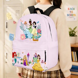 May include: A light purple backpack featuring illustrations of Disney princesses. The backpack has a front pocket with a zipper and black shoulder straps. The top of the backpack has a floral design with three princesses. The bottom of the backpack has illustrations of other princesses and castles.
