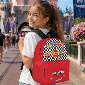 May include: A red backpack with a design from the Cars movie, featuring Lightning McQueen. The top section has a black and white chequered pattern with racing logos and the number 95. The bag has a black zip and straps.