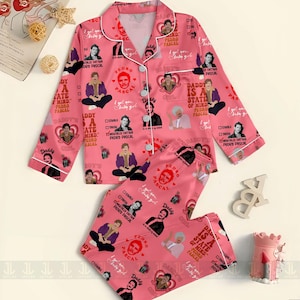 May include: Pink pajama set featuring a repeating pattern of Pedro Pascal's image, hearts, and text. The long-sleeved top has white trim and buttons. The pajama bottoms are long and have an elastic waistband. Text includes "Daddy is a state of mind" and "I got you baby girl."