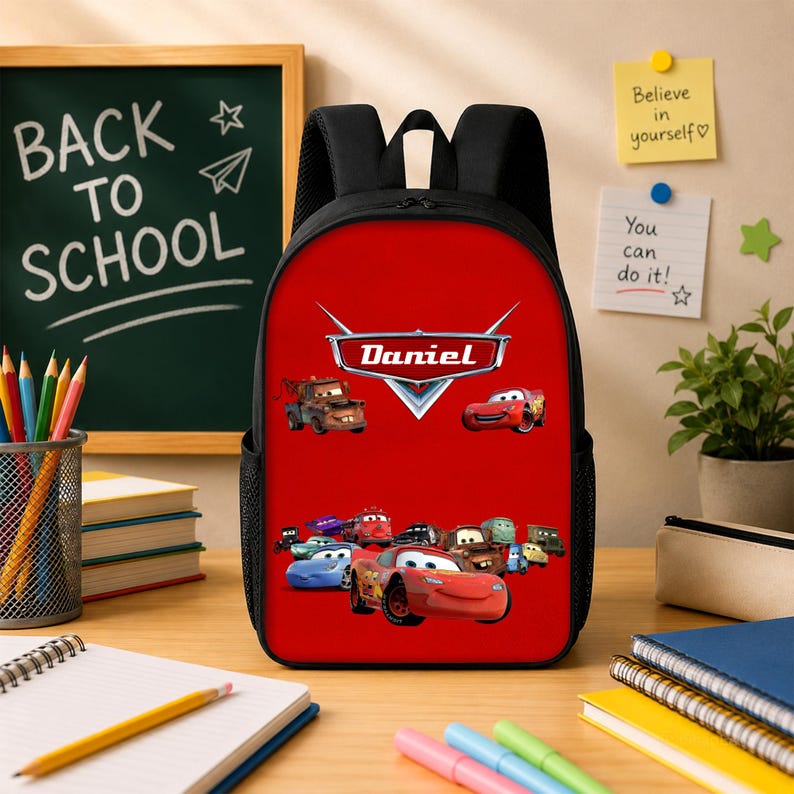 May include: A black backpack with a bright red front panel featuring a graphic of various animated race cars and the name Daniel printed in a stylised silver emblem. The backpack has black shoulder straps and side mesh pockets for storage.