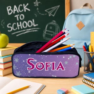 Pu&ograve; includere: Un astuccio viola con un design sfumato, fiocchi di neve bianchi e il nome Sofia stampato in grandi lettere rosa. L'astuccio &egrave; riempito con diverse matite colorate, tra cui rosso, bianco, giallo e blu, e ha una fodera interna scura.