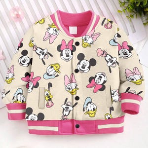 May include: A cream-coloured bomber jacket with a pink collar and cuffs. The jacket features a repeating pattern of cartoon characters, including Mickey Mouse, Minnie Mouse, Donald Duck, and Goofy.