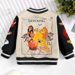 May include: A beige and black baseball jacket with a colorful Lion King graphic on the back. The graphic features Simba, Nala, Mufasa, and other characters from the Disney movie. The text "Disney The Lion King Est. 1994" is printed below the graphic.