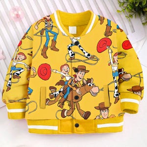 May include: Yellow bomber jacket with a repeating pattern of Woody and Jessie from Toy Story. The jacket has a white stripe around the collar and cuffs.