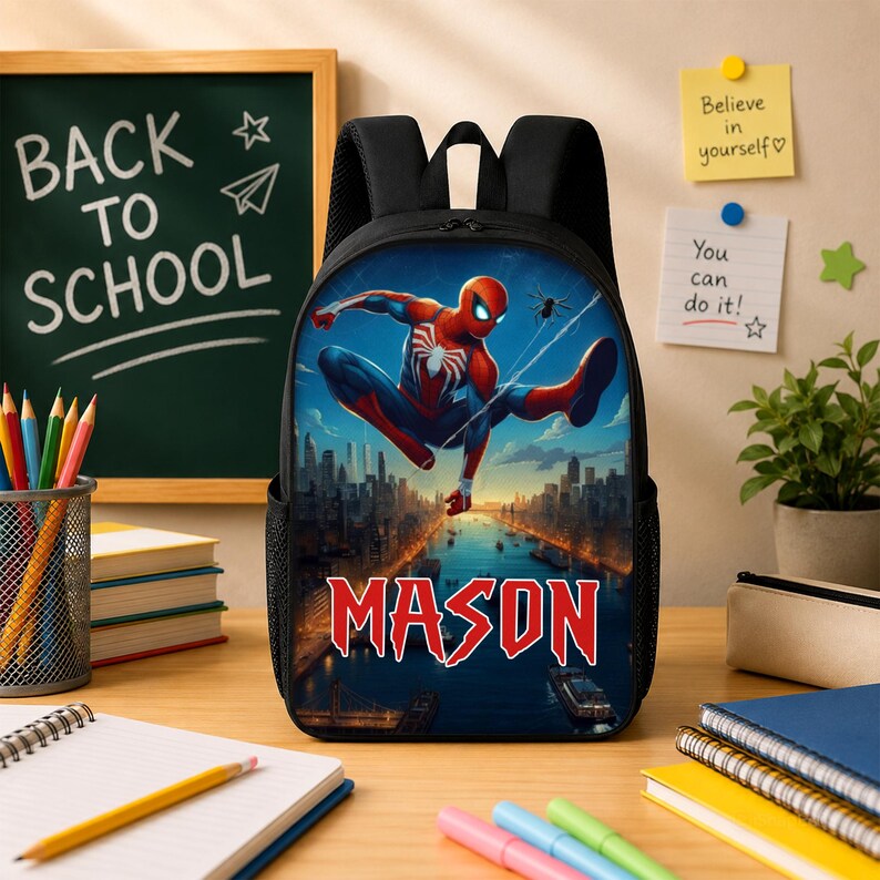 Puede incluir: Una mochila negra con un estampado gr&aacute;fico de un superh&eacute;roe con traje rojo y azul balance&aacute;ndose sobre el horizonte de una ciudad al atardecer. El nombre MASON est&aacute; impreso en letras rojas grandes en la parte inferior de la mochila.