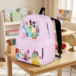 May include: A light purple backpack featuring illustrations of Disney princesses. The backpack has a black handle and straps, and a side pocket. The design includes images of princesses, flowers, and castles, with the words "Back to School" on a sign.
