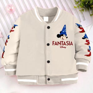 May include: A beige bomber jacket with a white collar and cuffs. The jacket features a Mickey Mouse character wearing a blue hat and the text "Fantasia Disney" on the front.