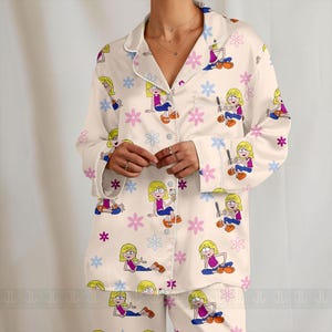 Pu&ograve; includere: Set pigiama color crema con personaggio dei cartoni animati e motivo floreale. La parte superiore a maniche lunghe ha una parte anteriore con bottoni e finiture bianche. I pantaloni abbinati completano il set. Il personaggio dei cartoni animati &egrave; raffigurato in varie pose.