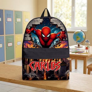 May include: A black backpack featuring a graphic of the superhero Spider-Man bursting through a brick wall on the top section. The bottom section displays a city skyline with fire and the name CARLOS printed in large, bold red letters.