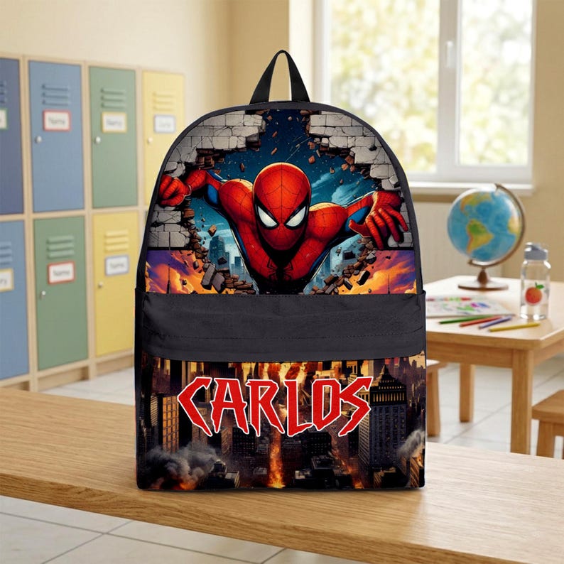 May include: A black backpack featuring a graphic of the superhero Spider-Man bursting through a brick wall on the top section. The bottom section displays a city skyline with fire and the name CARLOS printed in large, bold red letters.
