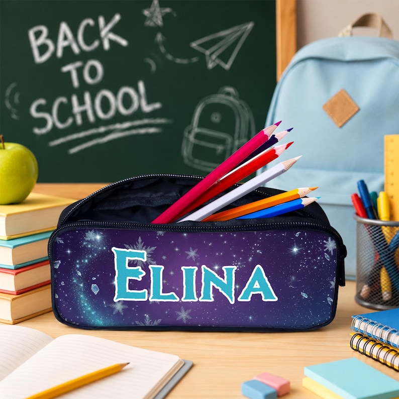 May include: A dark blue pencil case featuring a starry night sky pattern with white snowflakes and the name ELINA printed in large, light blue letters. The case is open and contains several colored pencils in red, white, yellow, and blue.