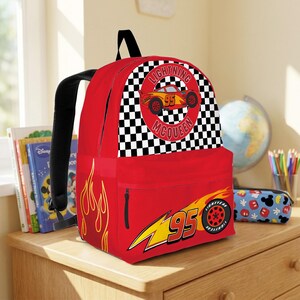 May include: A red Lightning McQueen backpack with a black checkered pattern and the words "Lightning McQueen" and "95". The backpack has a front pocket with a zipper and a side pocket.