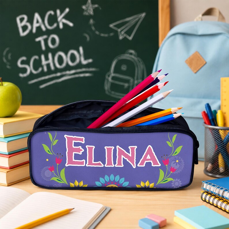 May include: A purple pencil case featuring the name ELINA in large pink letters, decorated with green vines and colorful floral motifs. The case is open and filled with several colored pencils, positioned on a desk with school supplies.