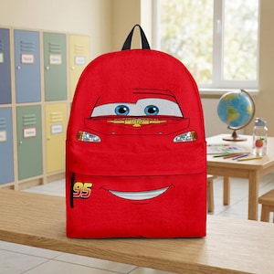Puede incluir: Una mochila roja con la cara de un coche de dibujos animados, con ojos azules y una boca sonriente. El n&uacute;mero "95" est&aacute; impreso en la parte inferior izquierda. Tiene un asa negra y es adecuada para la escuela o los viajes.