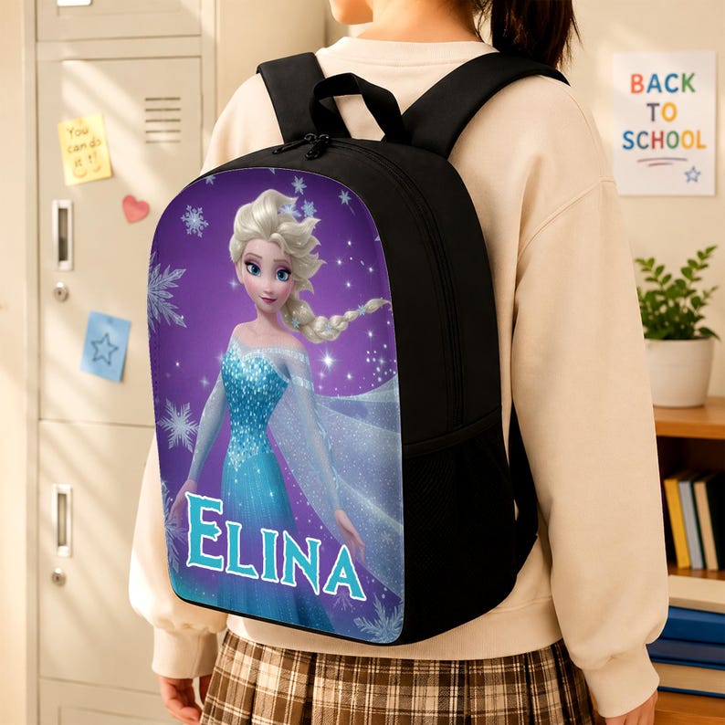 May include: A black backpack featuring a graphic print of a blonde character in a blue dress on a purple background with snowflakes. The name ELINA is printed in large white letters with a blue outline at the bottom of the graphic panel.