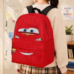 Puede incluir: Mochila roja con la cara de un coche de dibujos animados, ojos azules y una boca sonriente. El n&uacute;mero "95" est&aacute; en la parte inferior izquierda. Tiene correas negras para los hombros y un bolsillo delantero. El tema es la vuelta al cole.