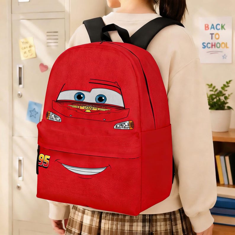 Puede incluir: Mochila roja con la cara de un coche de dibujos animados, ojos azules y una boca sonriente. El n&uacute;mero "95" est&aacute; en la parte inferior izquierda. Tiene correas negras para los hombros y un bolsillo delantero. El tema es la vuelta al cole.