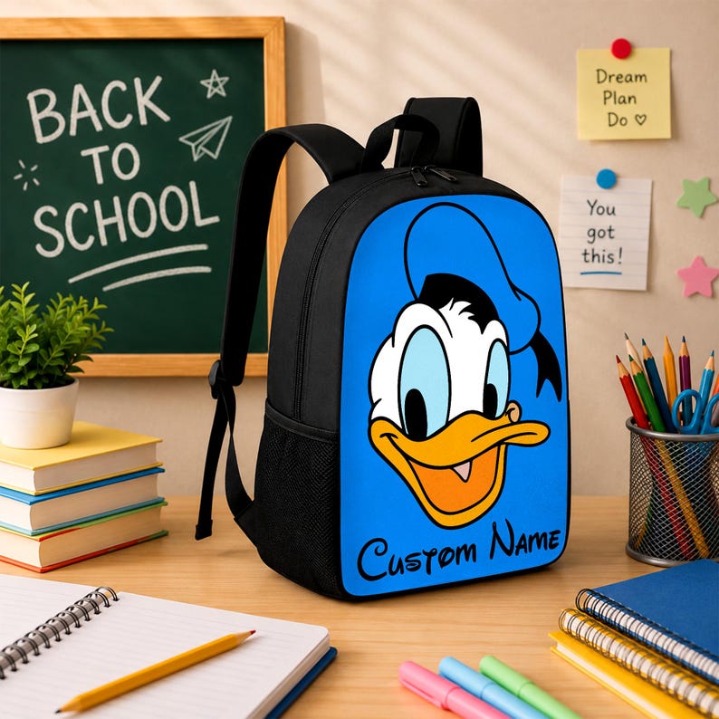 Peut inclure: Un sac &agrave; dos noir avec un panneau avant bleu vif orn&eacute; d'un grand graphique du visage de Donald Duck et du texte Custom Name imprim&eacute; en noir en dessous. Le sac &agrave; dos poss&egrave;de des bretelles noires et des poches lat&eacute;rales en filet.