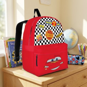 May include: A red backpack with Lightning McQueen's face on the front. The top section features a black and white chequered pattern with racing-themed patches. The backpack has black straps and a front zipped pocket, suitable for school or travel.