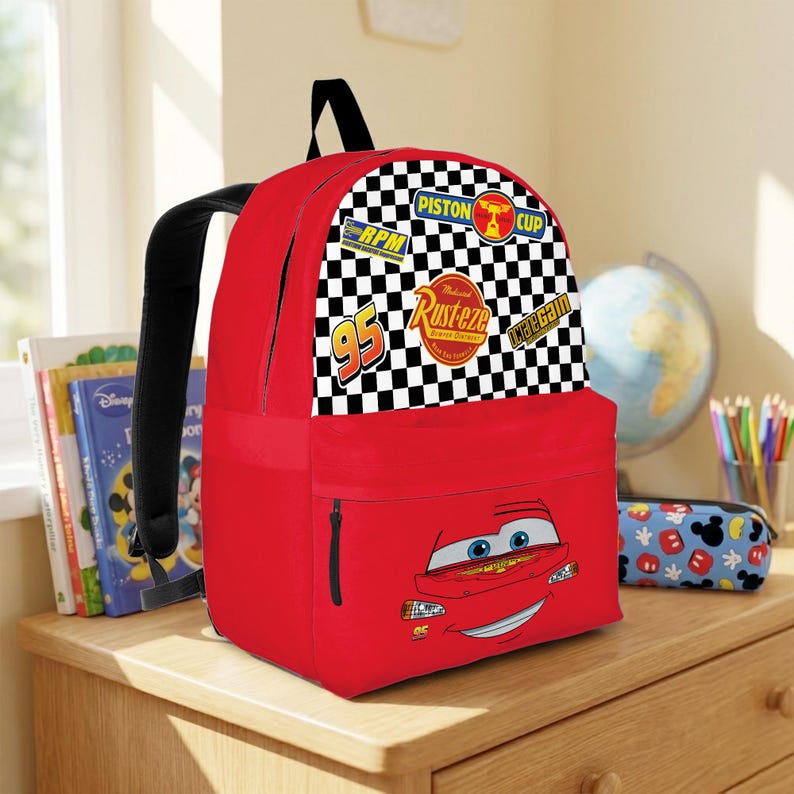 May include: A red backpack with Lightning McQueen's face on the front. The top section features a black and white chequered pattern with racing-themed patches. The backpack has black straps and a front zipped pocket, suitable for school or travel.