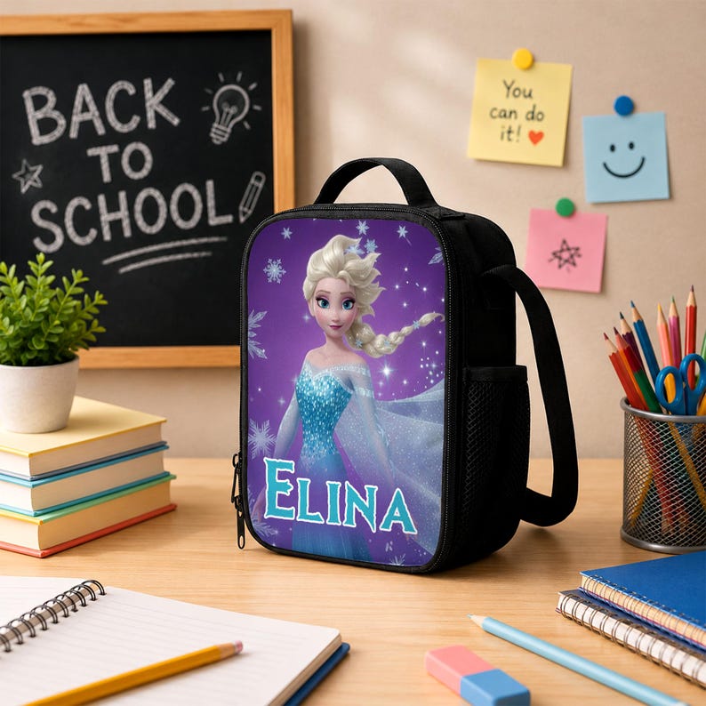 May include: A black lunch bag featuring a graphic of a blonde character in a blue dress with the name ELINA printed in light blue letters. The bag has a top handle, a zipper closure, and a side mesh pocket for storage on a desk surface.