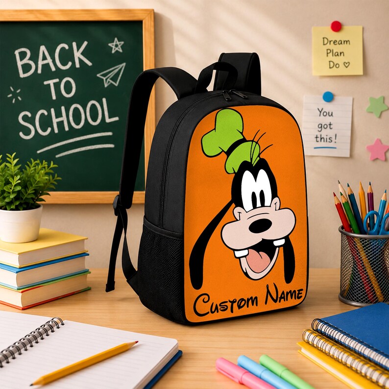 May include: A black backpack featuring a large orange front panel with a graphic of the cartoon character Goofy wearing a green hat. The text "Custom Name" is printed in black script at the bottom of the orange panel. The bag has black straps.