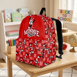 May include: Red Minnie Mouse backpack with a black handle and straps. The backpack features a large Minnie Mouse graphic and the words "MINNIE MOUSE". The body of the backpack is covered in a pattern of Minnie Mouse images and the words "MINNIE MOUSE".