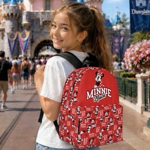 May include: A red Minnie Mouse backpack with a repeating pattern of Minnie Mouse illustrations and text. The backpack features a large Minnie Mouse graphic and the words "MINNIE Mouse" in white. The backpack is worn by a person.