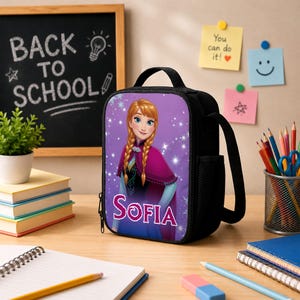 Pu&ograve; includere: Una borsa termica nera con la stampa di un personaggio dai capelli biondi intrecciati che indossa un mantello magenta e un abito blu, con il nome Sofia stampato in lettere bianche sotto il personaggio su uno sfondo viola con scintille bianche.