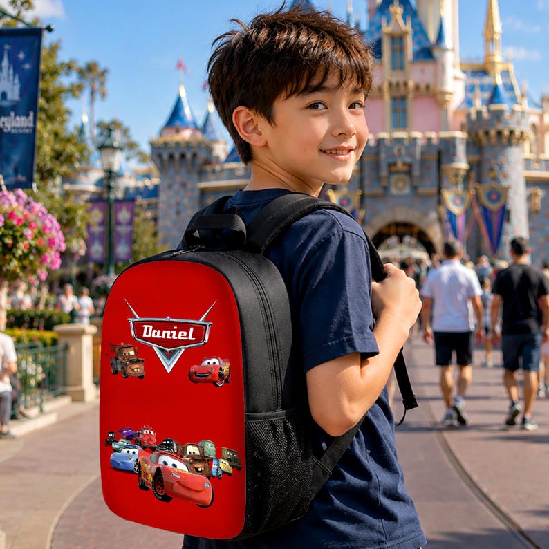 May include: A black backpack with a bright red front panel featuring a graphic print of various animated race cars and the name Daniel in a stylised white font. The backpack includes black side mesh pockets and adjustable shoulder straps.
