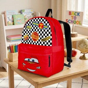 May include: Red backpack with a cartoon car design, a checkered flag pattern, and racing logos. It has a black handle and straps, plus a zipped front pocket. The words "Back to School" are visible in the background.