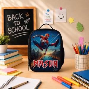 Puede incluir: Una bolsa de almuerzo rectangular negra con un gr&aacute;fico del superh&eacute;roe Spider-Man balance&aacute;ndose sobre el horizonte de una ciudad. El nombre MASON est&aacute; impreso en letras rojas grandes en la parte inferior. Tiene un asa superior y cierre de cremallera.