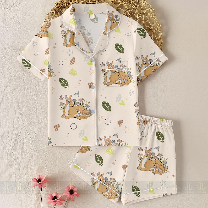 Op de afbeelding: Cr&egrave;mekleurige pyjamaset met een Bambi en Stampertje print. De top met korte mouwen heeft een reverskraag en een voorzak. De shorts hebben een elastische tailleband. De set is versierd met bladeren, bloemen en sterren.