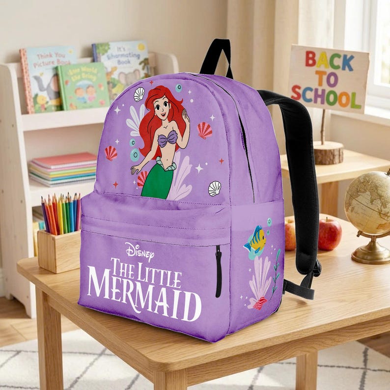 May include: A purple backpack featuring Ariel from Disney's The Little Mermaid. The backpack has a front pocket with a zipper, black straps, and a "Back to School" sign in the background. The backpack has a picture of Ariel, seashells, and a fish.