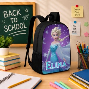 May include: A black backpack featuring a graphic print of a blonde character in a blue dress with the name ELINA printed in white letters. The backpack has a top handle, adjustable shoulder straps, and a side mesh pocket on a purple background.