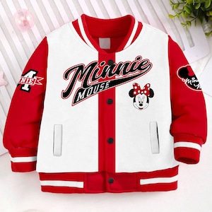 May include: A white and red baseball-style jacket with a Minnie Mouse design. The jacket has a red collar, red sleeves, and a white body with a red stripe down the center. The jacket has a zipper closure and a button-up front. The jacket has a Minnie Mouse graphic on the front with the text "Minnie Mouse" in black lettering. The jacket has a red and white striped trim around the sleeves and bottom.
