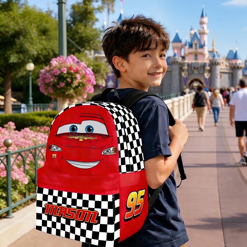 Peut inclure: Sac &agrave; dos rouge repr&eacute;sentant Flash McQueen du film Cars. Le sac &agrave; dos a un motif &agrave; carreaux sur les c&ocirc;t&eacute;s et le num&eacute;ro "95". Le nom "MASON" est imprim&eacute; sur le devant. Le sac &agrave; dos est port&eacute; par une personne.